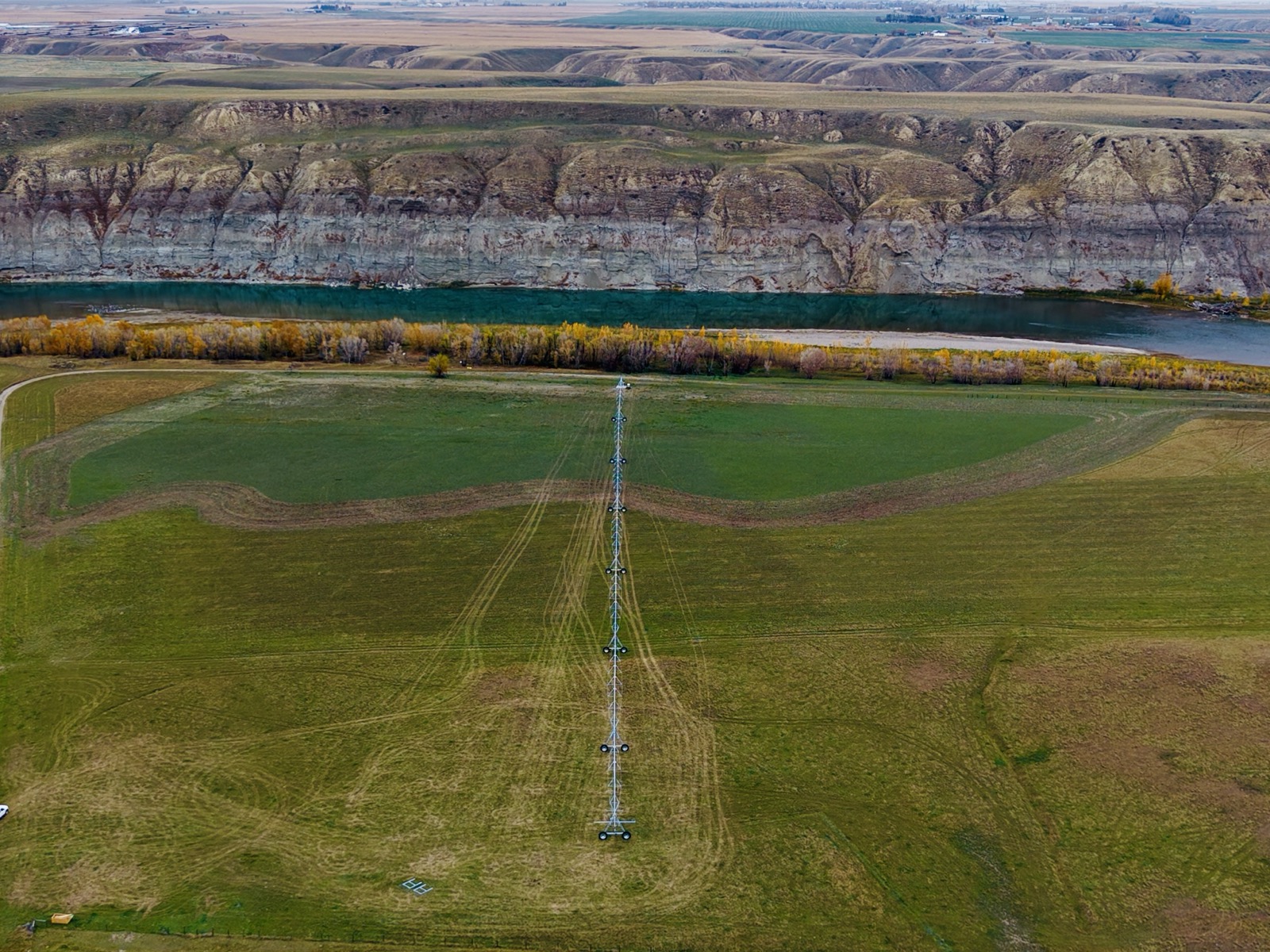 Aerial view along a centre pivot toward the Oldman River, autumn trees and exposed valley cliffs.